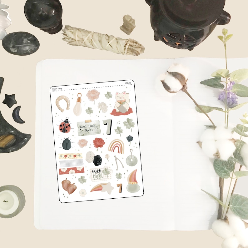 May include: A sheet of stickers with a variety of good luck charms, including a horseshoe, a four-leaf clover, a rainbow, a dice, a wishbone, a lucky cat, and a ladybug. The stickers are in a variety of colors, including red, green, blue, and yellow. The text "Good Luck Spell" is included on one of the stickers.