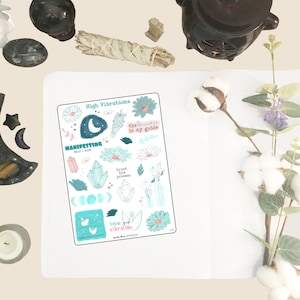 May include: A sticker sheet with a teal and white design, featuring the text "High Vibrations" and "Manifesting What I Want." The sheet includes illustrations of crystals, flowers, moons, and the phrase "trust the process."