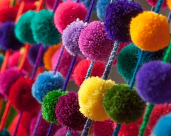 May include: A colourful garland of fluffy pom-poms in various colours, including red, orange, yellow, green, blue, purple, and pink.
