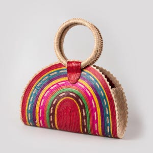 May include: A half-circle straw bag with a rainbow design and a red leather handle.