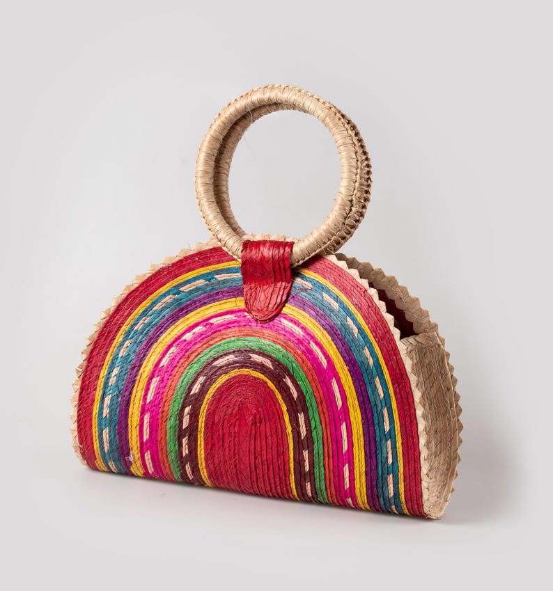 May include: A half-circle straw bag with a rainbow design and a red leather handle.