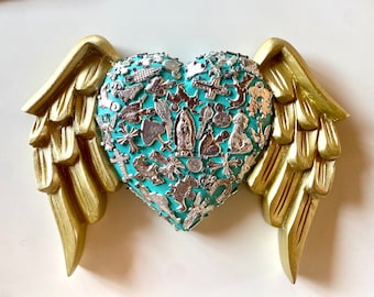 May include: A turquoise heart covered in silver charms and religious icons, with gold wings on either side.
