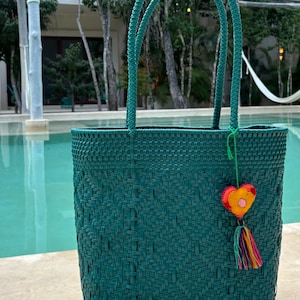 May include: Teal woven tote bag with double handles and a colourful heart-shaped charm with a tassel.