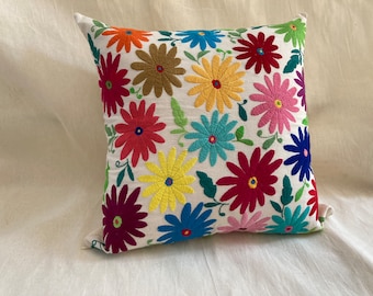 May include: A white pillow with colorful embroidered flowers. The flowers are in shades of red, pink, yellow, blue, and green.