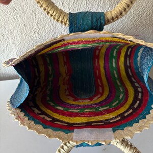 May include: A woven straw bag with a blue, yellow, red, green, and purple striped interior. The bag has two large, circular handles.
