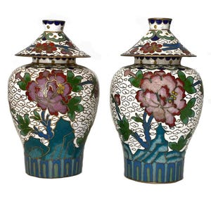 May include: Two decorative cloisonné vases with lids. The vases feature a white background with a cloud pattern and a large pink and purple flower design. The lids and bases have blue, green, and gold accents.