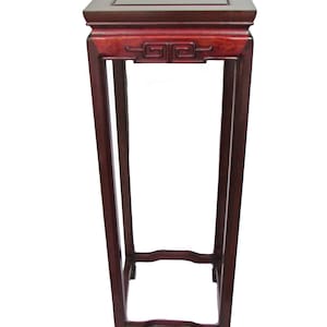 Può includere: Un alto portavasi in legno rosso scuro con piano quadrato e intagli intricati. Il portavasi ha un design semplice ed elegante ed è perfetto per esporre piante o altri oggetti decorativi.