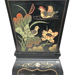 Può includere: Un armadio di legno nero con un design decorativo di uccelli e fiori. L'armadio ha una forma quadrata con una base rialzata e quattro gambe.