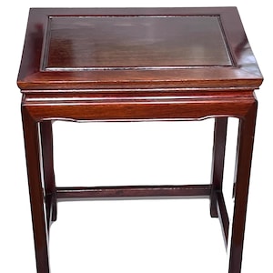 May include: A square, dark reddish-brown wooden side table with a glossy finish. The table has a rectangular top with a recessed center and four straight legs. The legs are connected by a lower horizontal support.