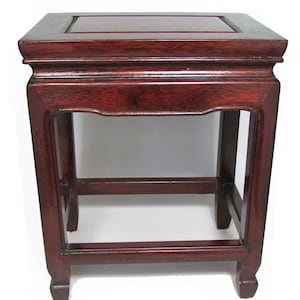 Può includere: Un tavolino da salotto in legno rosso scuro con piano quadrato e un ripiano. Il tavolino ha un design semplice con un bordo superiore leggermente curvo e quattro gambe.