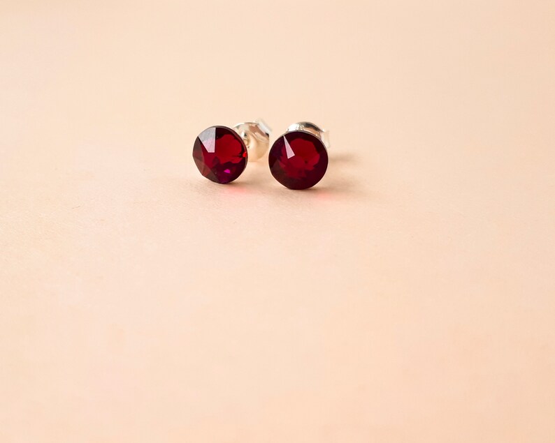 May include: A pair of silver stud earrings with red crystal stones.