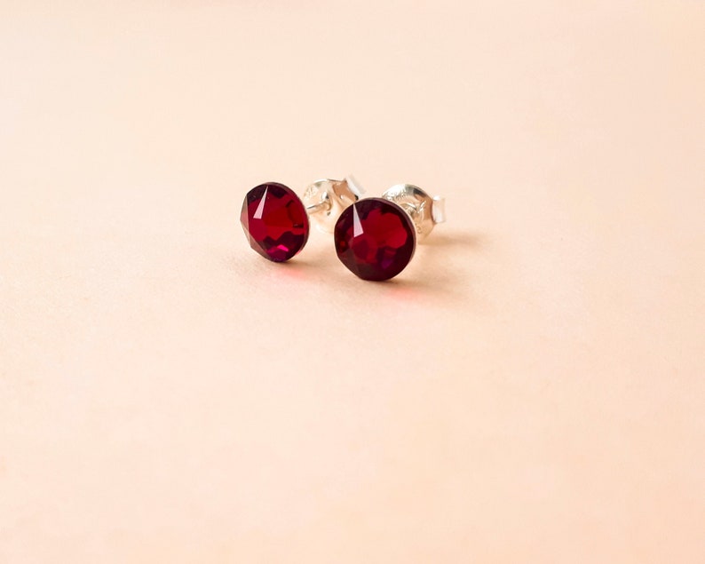 May include: A pair of silver stud earrings with small, round, dark red gemstones.
