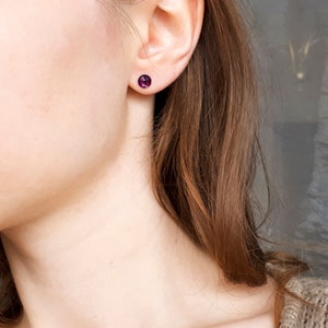 May include: A close-up of a person's ear with a small purple gemstone stud earring.