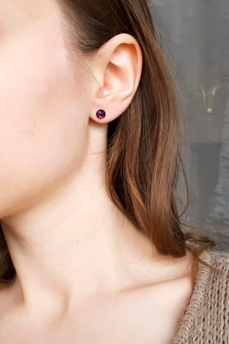 May include: A close-up of a person's ear with a small purple gemstone stud earring.