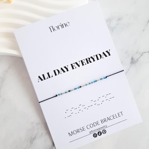 Op de afbeelding: Een witte kaart met de tekst "florine" bovenaan en "ALL DAY EVERYDAY" in vetgedrukt zwart eronder. Een blauw koordarmband met blauwe en gouden kralen wordt op de kaart getoond. Het armband is een morsecode armband met de code die onder het armband wordt weergegeven. De tekst onder de code luidt "MORSE CODE BRACELET" en "@florinejewelry".
