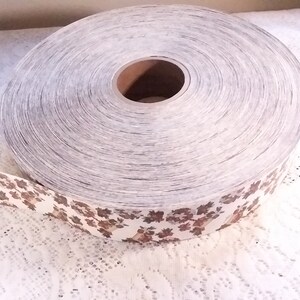 May include: A roll of white and brown patterned wallpaper with a floral design. The wallpaper is rolled up on a cardboard core.