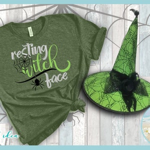 May include: Green t-shirt with the text "resting witch face" in black and green lettering. A green witch hat with black spiderweb design is next to the shirt.