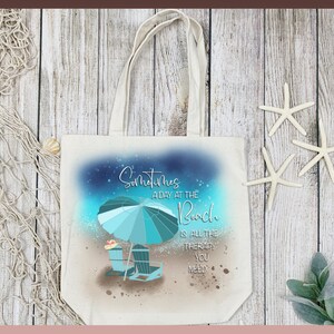 May include: A white canvas tote bag with a blue and green beach scene and the text "Sometimes a day at the beach is all the therapy you need".