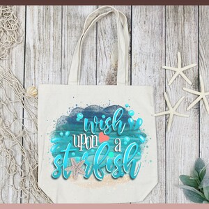 May include: A white canvas tote bag with a blue and green watercolor design of ocean waves and a starfish. The text "wish upon a starfish" is written in blue and green lettering.