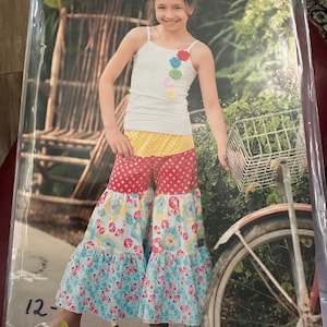 May include: A pattern package for children's clothing, featuring a girl wearing a white tank top with floral accents and patchwork gaucho pants. The package is labeled "Pink Fig Patterns" and includes the text "Lilous market day gaucho's no. 31".