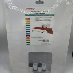 May include: A white Simplicity Rotary Cutting Machine Extension Table in plastic packaging. The label shows the product name, a 12 x 16 inch size, and an illustration of the table with a cutting machine. Four white and black feet are included.
