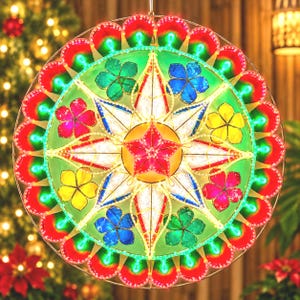 May include: A circular decorative lantern featuring a central red star surrounded by white star-shaped points and colorful flower motifs in blue, green, yellow, and pink. The outer edge is lined with a scalloped border of red and green lights.