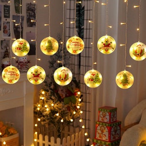 May include: A string of Christmas lights with round, illuminated ornaments. Each ornament features festive designs like Santa Claus, Christmas trees, and reindeer. The ornaments are lit with warm white lights, creating a cozy holiday atmosphere.