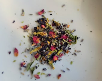 May include: A mix of dried flowers and herbs, including lavender, rose petals, and blue cornflowers. The mixture is a light purple, pink, and yellow color.
