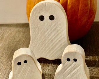 Könnte beinhalten: Drei weiße Holz-Geisterfiguren mit schwarzen Augen. Der größte Geist steht hinter den beiden kleineren Geistern.