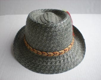 May include: A gray woven straw hat with a decorative band and a colorful feather accent. The hat has a round crown and a wide brim. The band is a woven pattern of tan, red, and black.