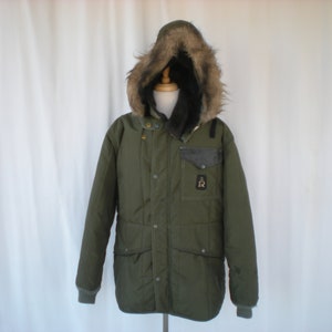 May include: A green hooded winter jacket with a fur-lined hood. The jacket has a large pocket on the left chest with a logo that says "R".