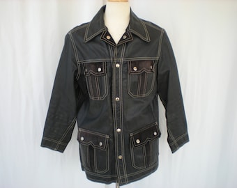 May include: A black leather jacket with brown suede accents and contrasting white stitching. The jacket has a button-up front closure, a collar, and two large pockets.