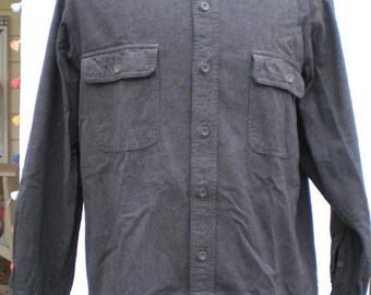 May include: A charcoal gray button-down shirt with two chest pockets. The long-sleeved shirt has a collared neckline and buttoned cuffs. The shirt is displayed on a mannequin.