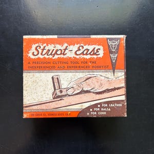 May include: Vintage "Stript-Ease" precision cutting tool box. The orange and white box features the product name and a diagram of the tool in use. Text indicates it's for leather, balsa, and cork. Made by The Carvir Co., Hermosa Beach, Calif.