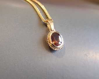 Yellow gold peach tourmaline pendant in 14k yellow gold with dotted ornamental edge. Possibly with necklace.