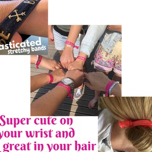 May include: Pink elastic hair ties and bracelets with the text "elasticated stretchy bands" on a black band. The hair ties are shown in a bun and on wrists.