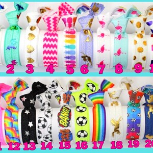 K&ouml;nnte beinhalten: Eine Sammlung von zwanzig bunten Haargummis mit verschiedenen Mustern und Designs. Die Designs umfassen Einh&ouml;rner, Herzen, Zickzackmuster, Ananas, Flamingos, Punkte, Fu&szlig;b&auml;lle, Sterne, Regenbogen und goldene Silhouetten. Jedes Haarband hat eine andere Farbe.