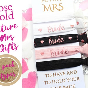 May include: Three pink and black elastic hair ties with the word "Bride" in rose gold lettering. The hair ties are packaged with a white card that reads "To have and to hold your hair back".