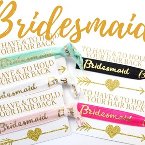 May include: Four hair ties with the text "To Have & To Hold Your Hair Back" and the word "Bridesmaid" printed on them. The hair ties are in the colors pink, white, black, and teal.