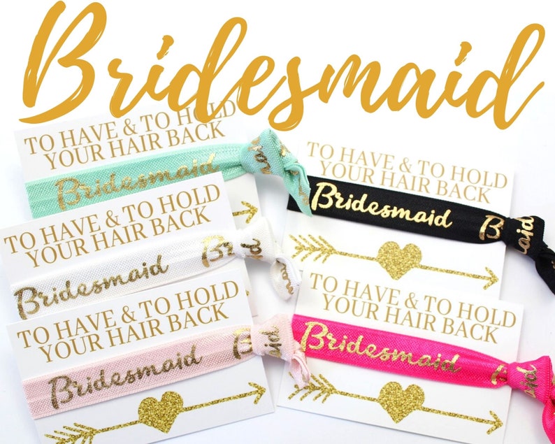 May include: Four hair ties with the text "To Have & To Hold Your Hair Back" and the word "Bridesmaid" printed on them. The hair ties are in the colors pink, white, black, and teal.