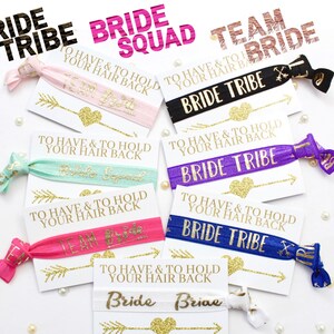 May include: A set of eight colorful hair ties with gold glitter and text that says "Bride Tribe" and "Team Bride". The hair ties are packaged with small cards that say "To have and to hold your hair back".