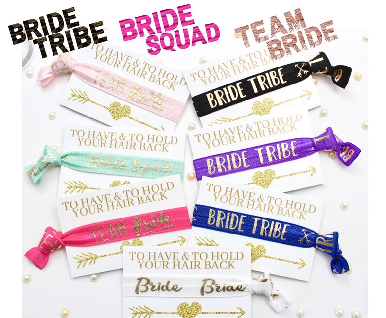 May include: A set of eight colorful hair ties with gold glitter and text that says "Bride Tribe" and "Team Bride". The hair ties are packaged with small cards that say "To have and to hold your hair back".