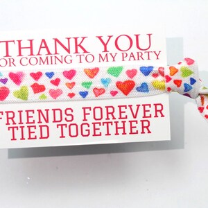 May include: White card with the text "Thank you for coming to my party" and "Friends forever tied together". A white elastic hair tie with colorful hearts is attached to the card.