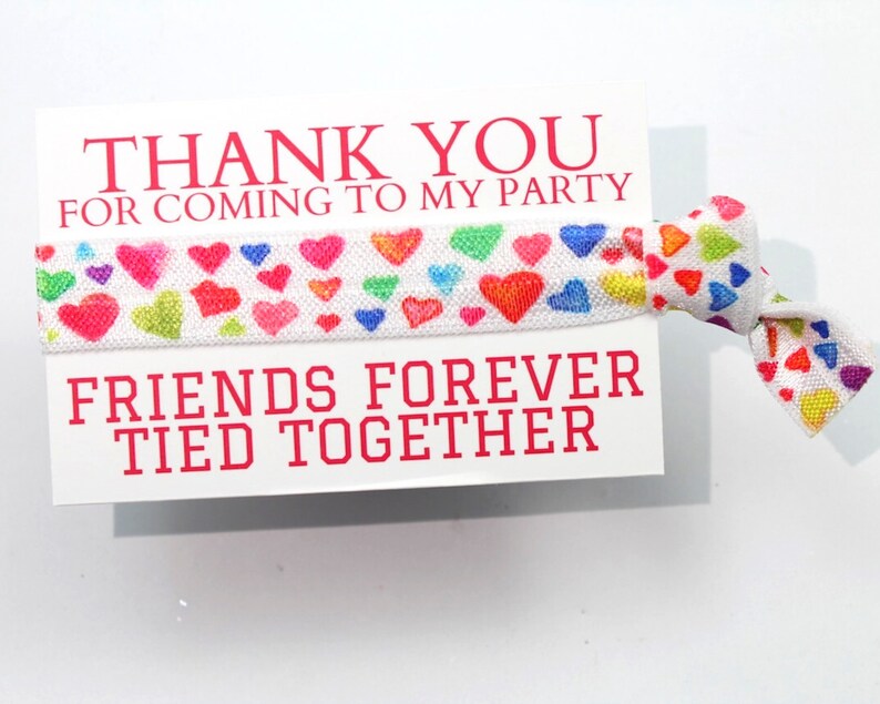 May include: White card with the text "Thank you for coming to my party" and "Friends forever tied together". A white elastic hair tie with colorful hearts is attached to the card.