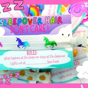 K&ouml;nnte beinhalten: Ein Geschenkset zum Thema Pyjamaparty mit einem wei&szlig;en elastischen Haargummi, verziert mit bunten Einhorn-Applikationen. Das Set enth&auml;lt eine Karte mit dem Text "SLEEPOVER HAIR DON'T CARE!" und "RULES". Der Hintergrund ist rosa.
