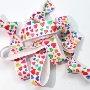May include: A set of colorful hair ties with a white background and a rainbow heart pattern.