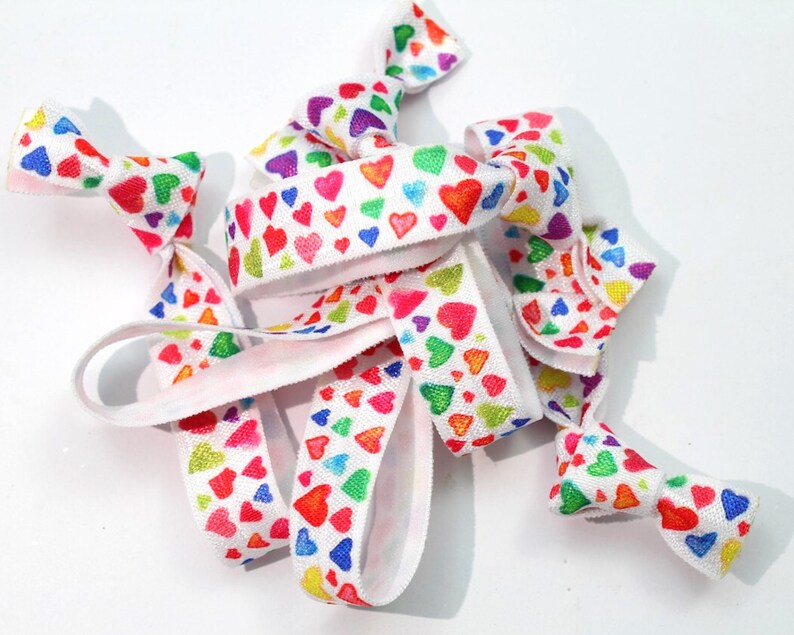 May include: A set of colorful hair ties with a white background and a rainbow heart pattern.