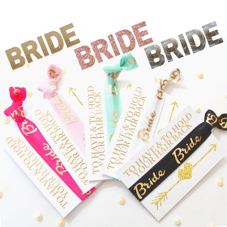 May include: Five hair ties with cards that say "To Have & To Hold Your Hair Back" in gold lettering. The hair ties are pink, blue, white, black, and a glittery gold heart with an arrow.