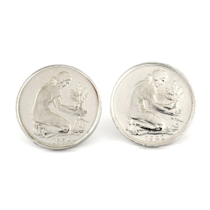 Könnte beinhalten: Zwei silberfarbene Manschettenknöpfe mit detailliertem Reliefdesign. Jeder Manschettenknopf zeigt eine kniende Figur, die eine Pflanze pflegt, mit der Jahreszahl 1994. Die Manschettenknöpfe sind kreisförmig und haben eine polierte Oberfläche.