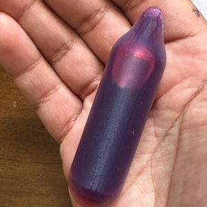 Op de afbeelding: Een doorschijnend paars cilindrisch object met een afgeronde punt en basis. Het object wordt in een hand gehouden en de binnenkant heeft een roodachtige tint. Het object lijkt van een vast materiaal te zijn gemaakt.